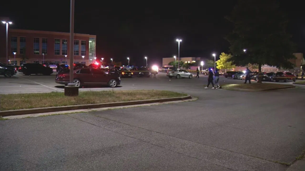 Picture of school parking lot with multiple cars and people walking.
