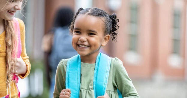 This is an up close photo of a young girl with pigtails wearing her blue backpack.