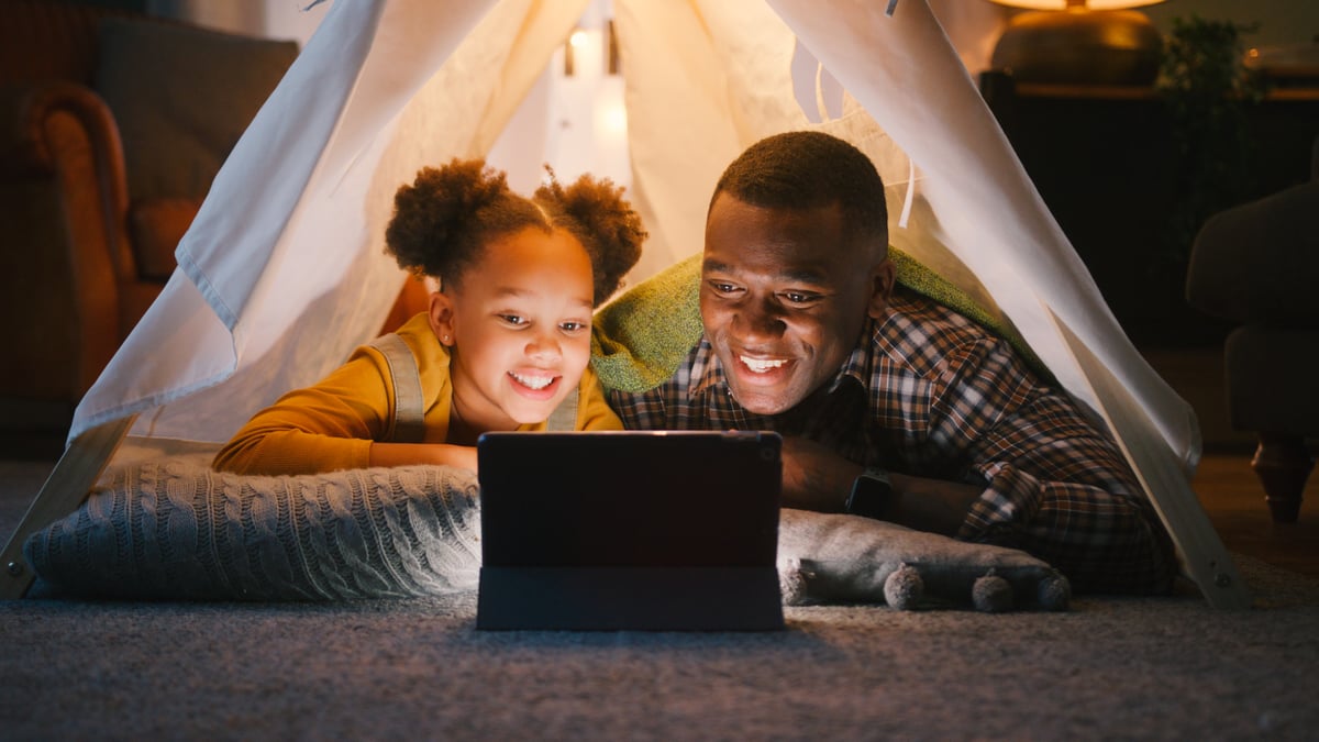Dad and daughter watching screens in an indoor tent